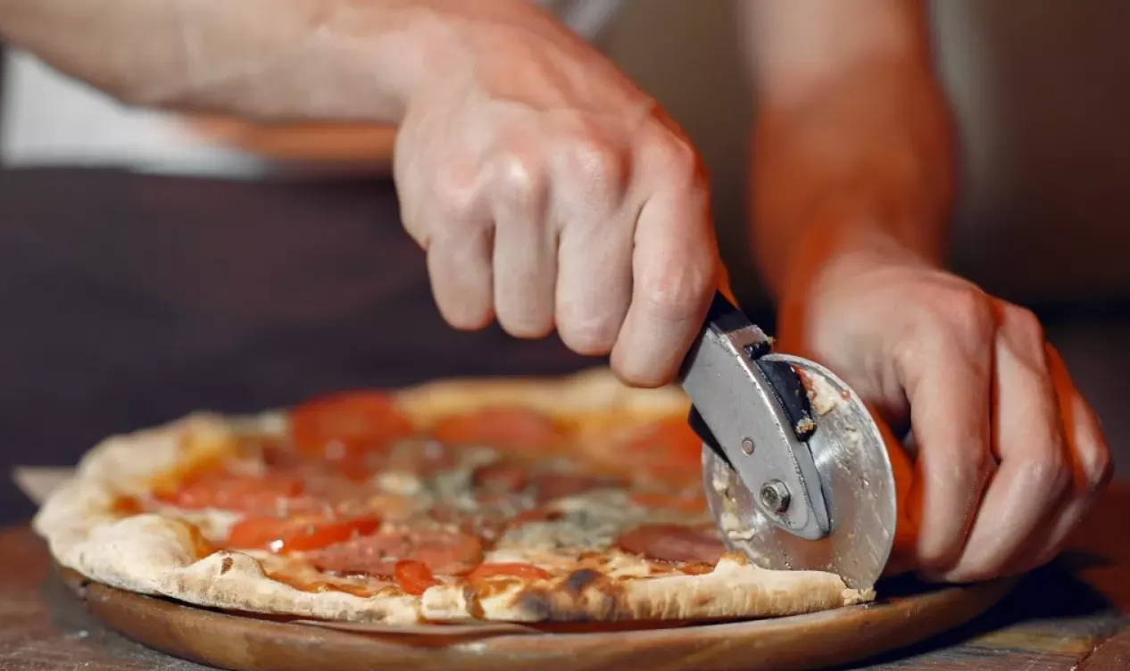 Pizza recién cortada en porciones sobre tabla de madera